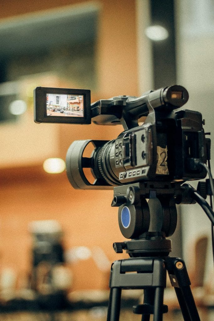 Professional video camera on tripod capturing a scene indoors, focusing on a display screen.