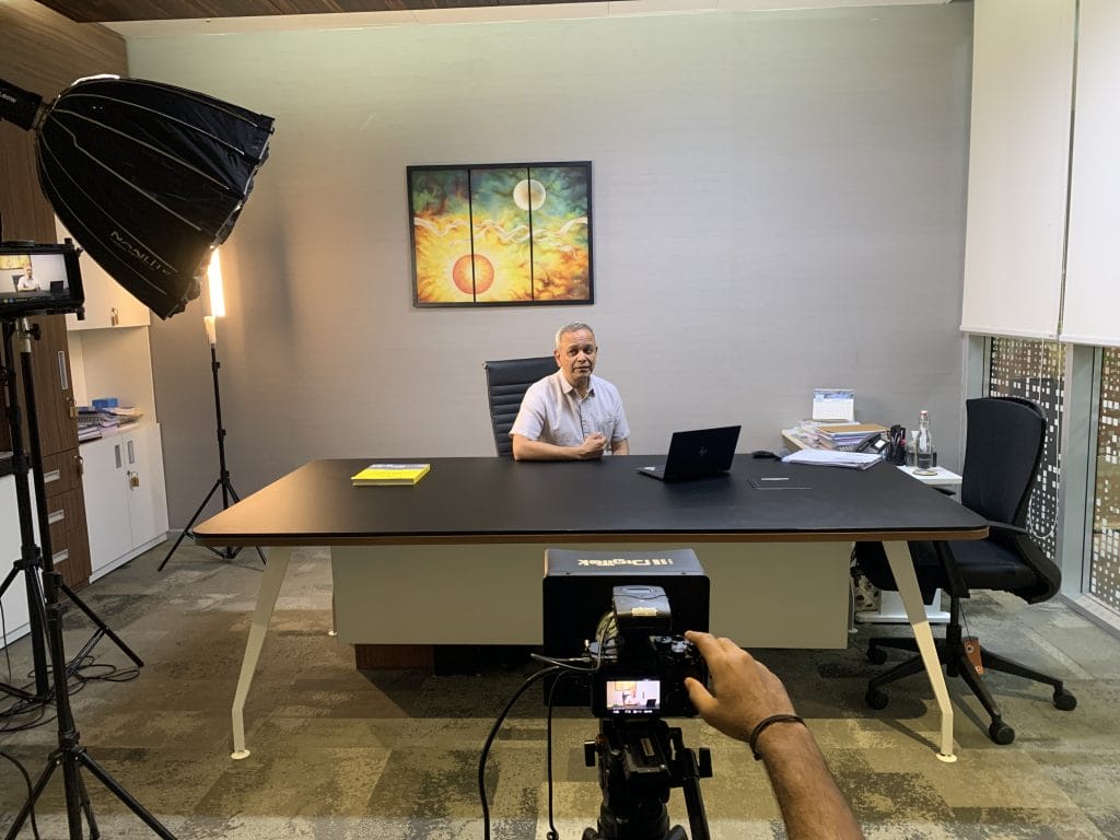 Man in an office setting recording a video with professional lighting and camera equipment.